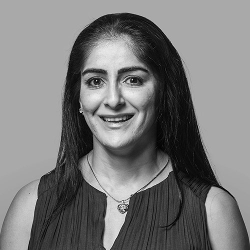 Smiling South Asian woman with long dark hair wearing a black sleeveless top, with a friendly expression.