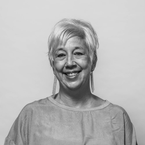Smiling middle-aged woman with short, light-coloured hair wearing a loose-fitting gray blouse.