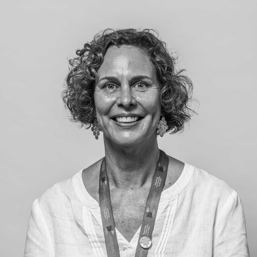 Woman with curly hair, smiling, wearing a white blouse and a colorful lanyard.