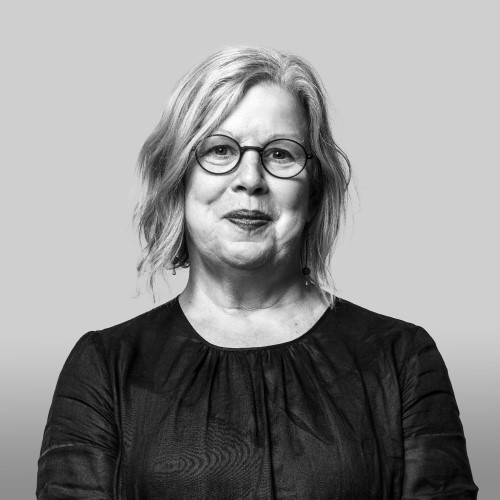 A middle-aged woman with light brown hair wearing glasses and a black blouse, smiling softly at the camera.