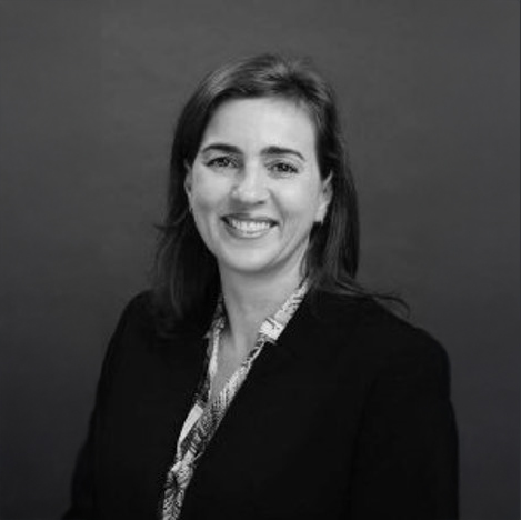 Professional woman smiling in a black blazer with a patterned blouse, with a confident expression.
