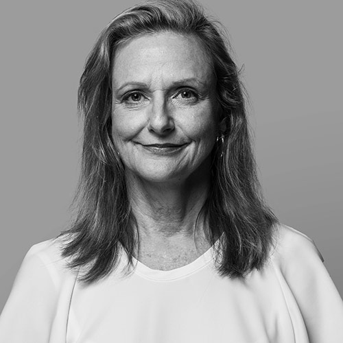 A woman with long, light brown hair, wearing a white blouse, smiling softly.